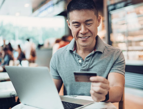 A man sitting down at a laptop with a credit card in one hand