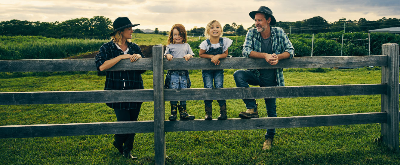 A young rural family leaning against a wooden fence in a large field